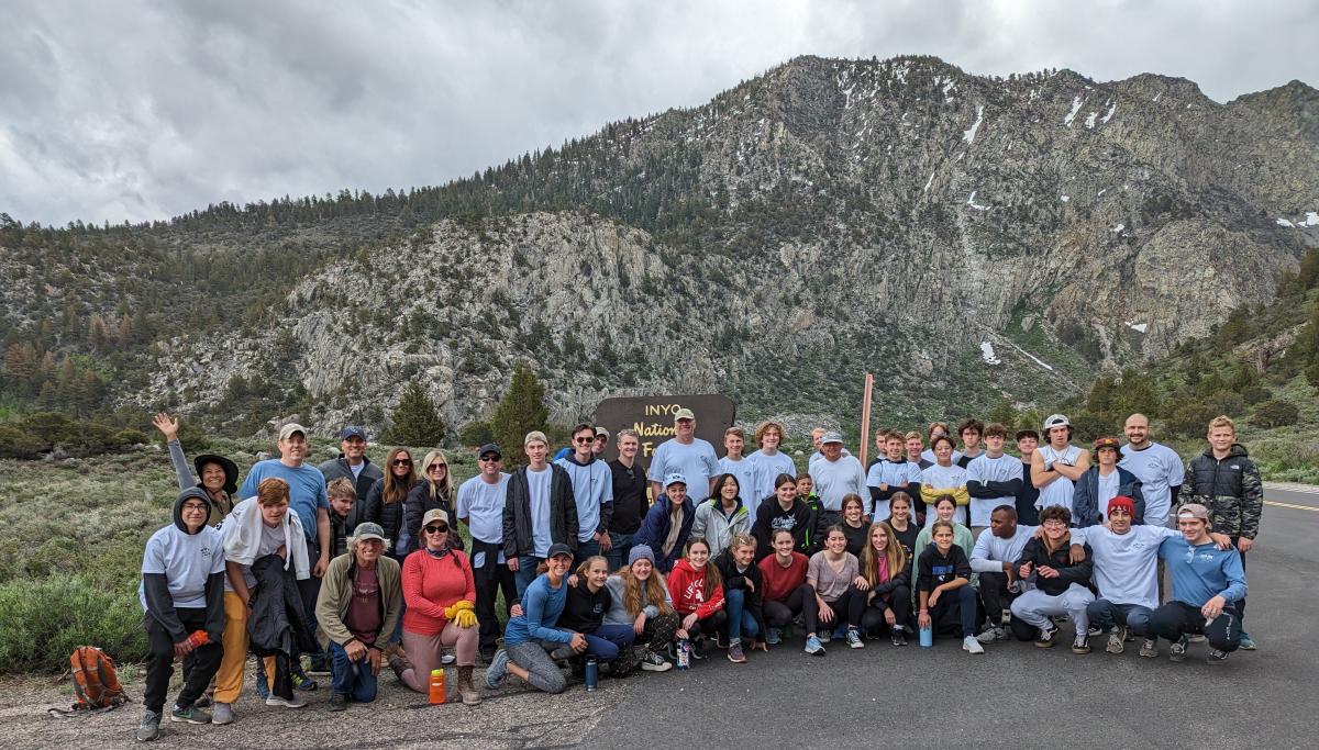 Image of a large group of adult and youth volunteers posing for a group picture in front of a mountain backdrop. 